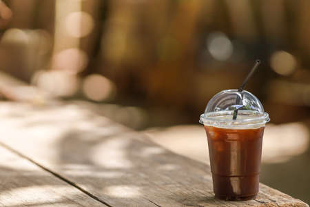 Closeup of takeaway plastic cup of iced black coffee Americano on wooden table with copy space.の写真素材
