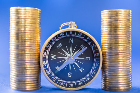 Money, Business and Direction and Planning Concept. Closeup of compass with two stack of gold coins...