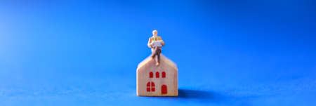 Business, Mortgage and Home Loan and information Cover page Concept. Close up of businessman miniature figure people sitting and reading a book on wooden home toy with blue background.の写真素材