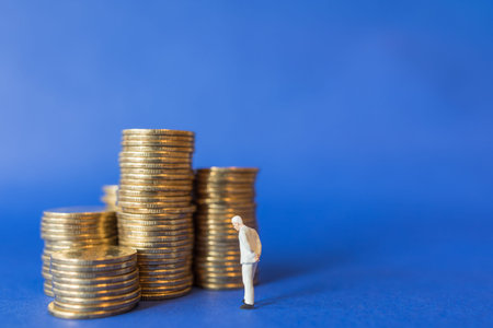 Business, Money Investment and Planning Concept.  Close up of businessman miniature people figure standing with stack of gold coins on blue background with copy sapce.の写真素材