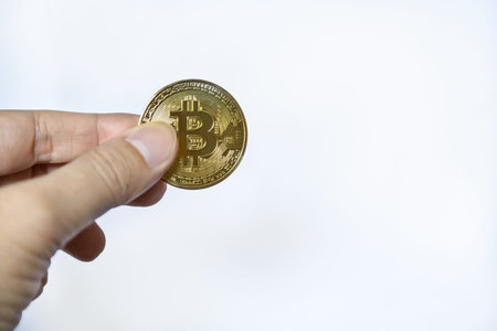 Digital Money and Cryptocurrency Concept. Closeup of gold bitcoin coin on mand hand on white...