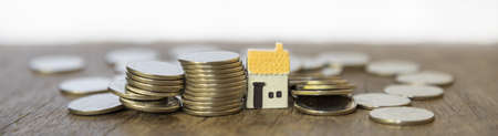 Business, Mortgage, Home Loan Cover Page Concept. Closeup of three mini house toy with stack and pile of coins on wooden table.の写真素材