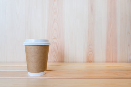Closeup of takeaway paper cup of hot coffee on wooden table with copy space.