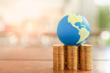 Global Business and Financial, Economic and palnning Concept. Close up of mini world ball on stack of gold coins on wooden table with copy space.の写真素材