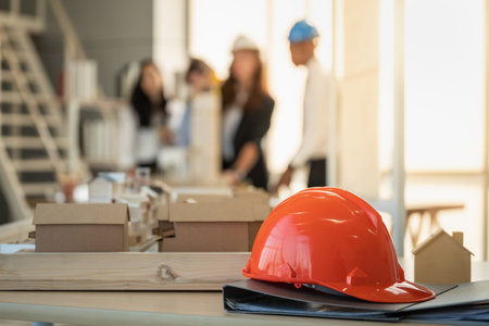 Closeup of orange hard safety helmet hat of workman as engineer on black folder with house model and...