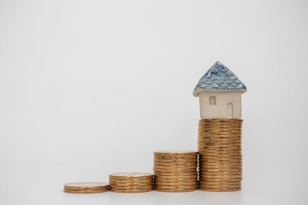 Business, Saving and Home Loan Concept. Closeup of house toy ceramic on top of stack of gold coins...
