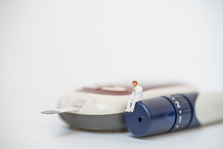 Doctor miniature figure sitting on lancet with glucose meter on white background using as diabetes,...