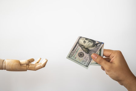 Money Financial and Payment Concept. Closeup of woman hand holding and give a 100 US Dollar bank note to wooden hand model.の写真素材
