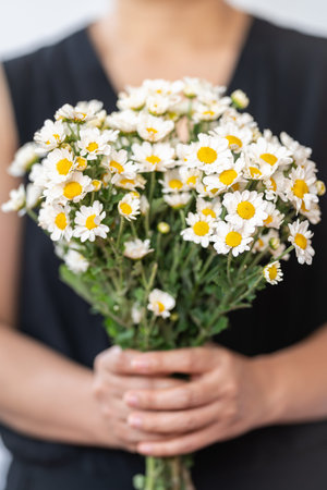 Woman wearing blck dress holding bunch of white Daisy flowers.