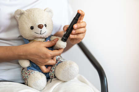 Close up of woman hands using lancet on teddy bear doll hand to check blood sugar level by Glucose meter. Use as Conceptual Medicine, diabetes, glycemia, health care and people concept.の写真素材