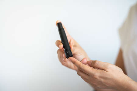 Close up of woman hands using lancet on finger to check blood sugar level by Glucose meter. Use as Medicine, diabetes, glycemia, health care and people concept.の写真素材