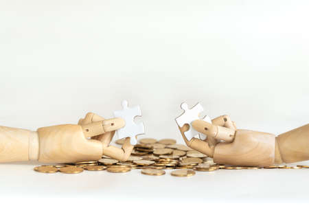 Money and Business Solution Concept. Closeup of wooden hand model holding puzzle jigsaw on pile of gold coins and white background.の写真素材