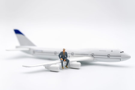 Business and Travel Concept. Businessman miniature figure people sitting on wing of airplane toy model on white background.の写真素材