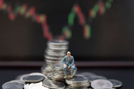 Business Money and Financial Concept.Businessman miniature figure people sitting on pile and stack of silver coins with candlestick chart as background.の写真素材