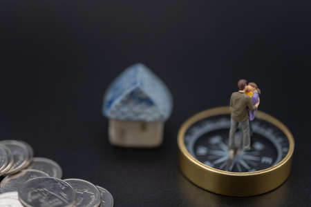 Money, Financial, Business and Family concept, Miniature figures man, woman and child stand on compass with mini house toy model and pile of silver coins on black background.の写真素材