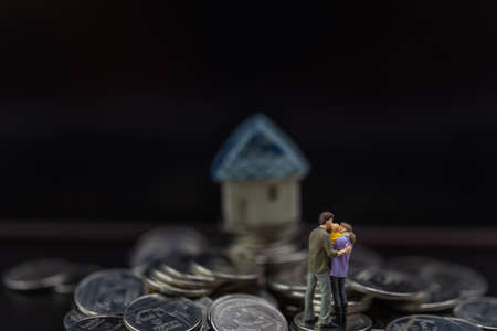 Money, Financial, Business and Family concept, Miniature figures man, woman and child stand on pile of coins with mini house toy model on black background.の写真素材