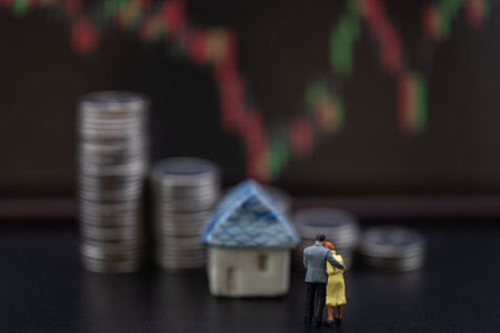 Money, Financial, Business Home Investment and Family concept, Miniature figures man and woman standing in front of mini house toy model and stack of silver coins with candlestick chart as background.の写真素材