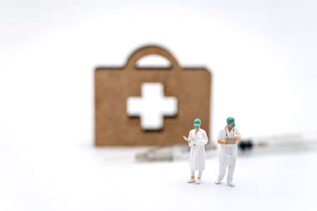 Healthcare and vaccine Consept. Two doctor miniature figure people with patient file standing with syringe and wooden bag with cross logo on white background.の写真素材