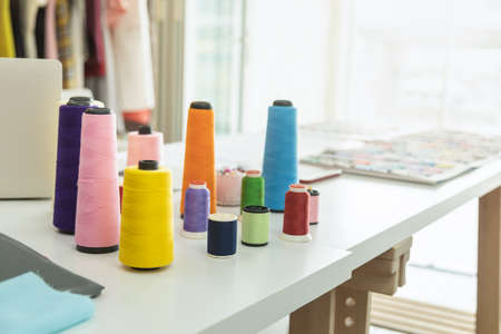Closeup of yellow and multicolor sewing threads on wooden white working table with cloth and dress in designer room studio.の写真素材