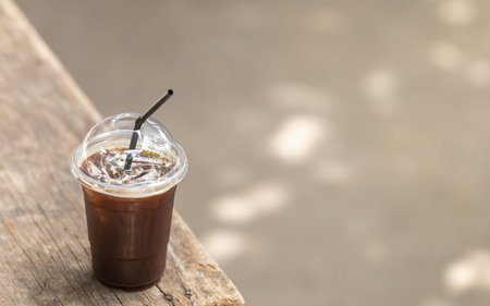 Closeup of take away plastic of iced black coffee Americano on old wooden table with copy space.