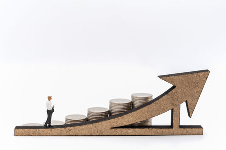 Business, Money Investment and Planning Concept. Businessman miniature figure people figure walking on wooden arrow sign with stack of silver coins on white background.の写真素材