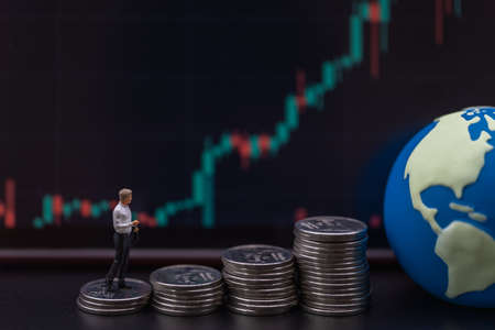 Business Money, Financial and Home Concept. Businessman miniature figure people walking on top of stack of silver coins with mini world ball and  candlestick chart as background.の写真素材