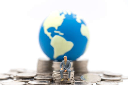 Business Money, Financial and Home Concept. Businessman miniature figure people sitting on top of stack and pile of silver coins with mini world ball on white background.の写真素材