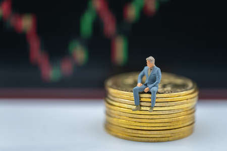 Business, Money, Cryptocurrency and Financial Concept. Businessman miniature figure sitting on stack of gold Bitcoin coins with candlestick chart as background.の写真素材