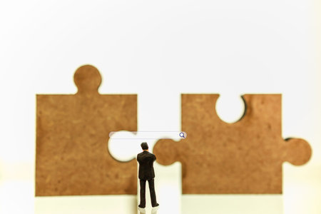 Business planning and solution Concept. Businessman miniature figure people standing and looking to tow pieces of wooden Jigsaw puzzle with search box iconの写真素材