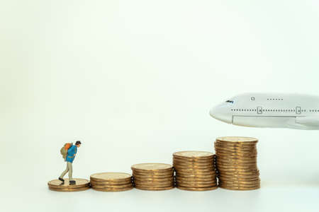 Business and Travel Concept. Traveler miniature figure people with backpack walking on top of stack of gold coins to mini airplane toy model.の写真素材