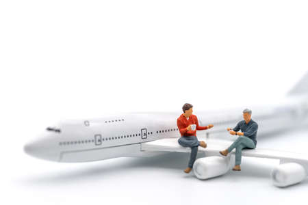 Travel Concept. Two man miniature figure people with cup of coffee sitting and talking on wing of airplane toy model on white background.の写真素材
