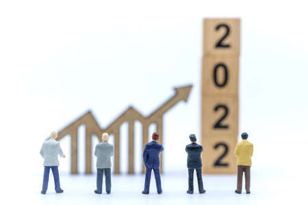 2022 New Year and Business Planning Concept. Closeup of group of businessman miniature figures standing and looking to wooden arrow chart sign and stack of wooden number block on white background.の写真素材