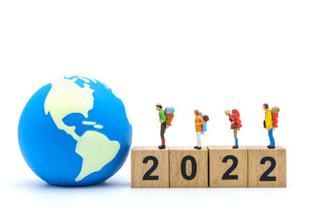 2022 New Year and Travel Concept. Closeup of group of traveler miniature figures with backpack standing on stack of wooden number block with mini world ball on white background.の写真素材
