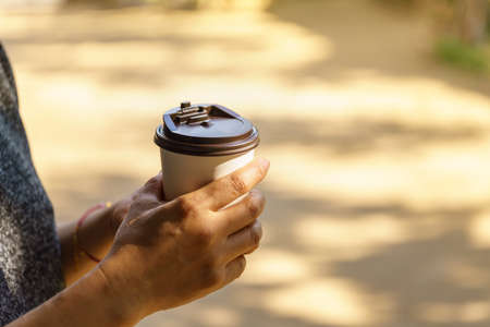 Closeup of woman hand holding disposable take away paper cup of hot coffee with copy space.の写真素材