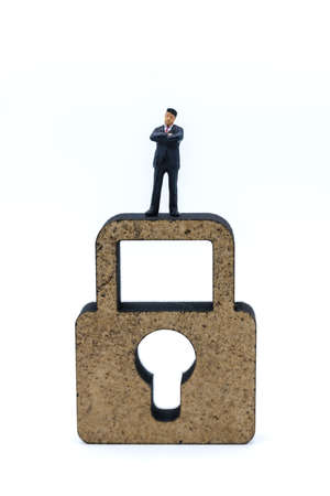 Money and Security Concept. Closeup of businessman miniature figure people standing on wooden master key lock icon on white background.の写真素材
