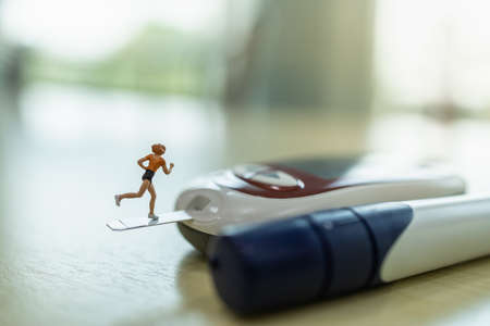 Woman runner miniature figure running on glucose meter with lancet on wooden table. Using as diabetes, glycemia, health care and people concept.の写真素材