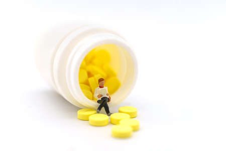 Healthcare, Medical and Information Concept. Closeup of businesswoman miniature figure sitting and reading book on bottle of yellow pills on white background.の写真素材