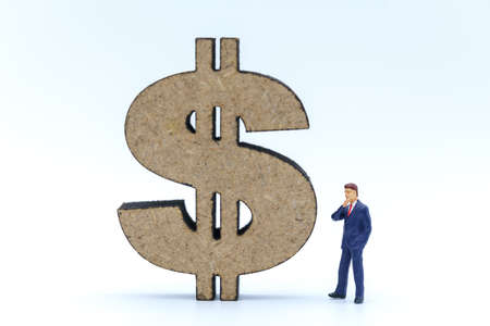 Business, Money Investment and Planning Concept. Businessman miniature figure people figure standing and looking to wooden US Dollar sign on white background.の写真素材