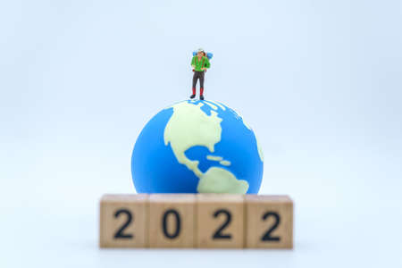 2022 New Year and Travel Concept. Closeup of male traveler miniature figures with backpack standing with stack of wooden number block and mini world ball on white background.の写真素材