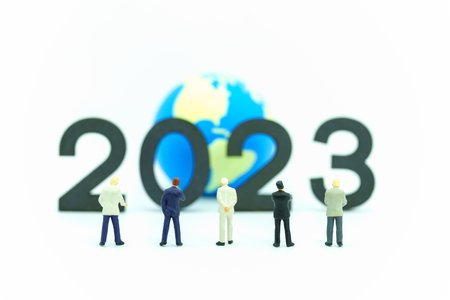 2023 Global Business New Year Concept. Closeup of group of businessman miniature figures standing and looking to number  and mini world ball on white background.の写真素材