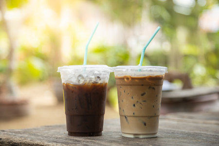 Closeup of takeaway plastic cup of iced black coffee Americano and coffee latte on wooden table with green nature background.の写真素材