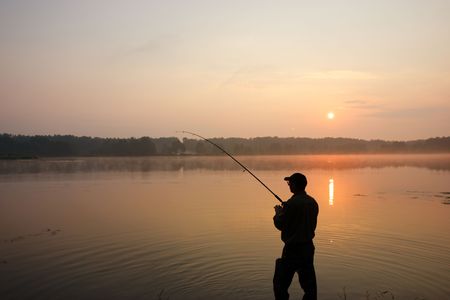 Silhouette of fisherman standing in a lake and catching the fish during sunriseの写真素材