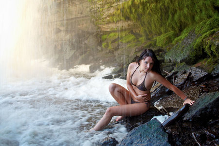 Young lady in bikini posing on stones under waterfallsの写真素材