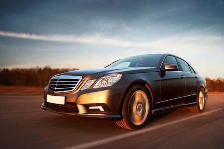New sporty car driving fast towards setting sun