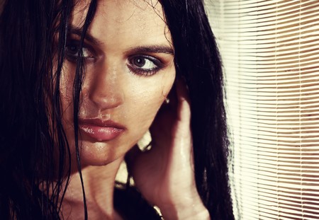 Sexy brunette woman with wet hair in the sunlight going through wooden jalousieの写真素材