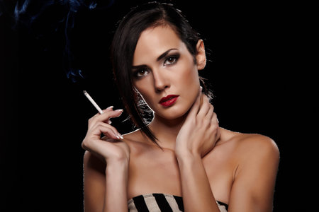 Elegant brunette woman smoking a cigarette on black backgroundの写真素材
