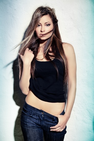 Glamorous young lady touching her hair near white wallの写真素材