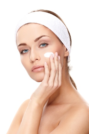Beautiful young woman applying a creme on her face isolated on white backgroundの写真素材