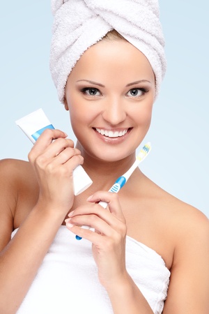 Young beautiful lady with a towel on her head showing toothpaste and brushの写真素材