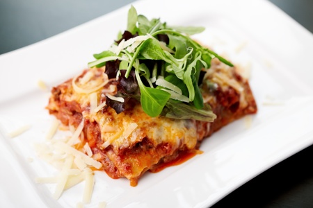Lasagna served on a white plate with saladの写真素材